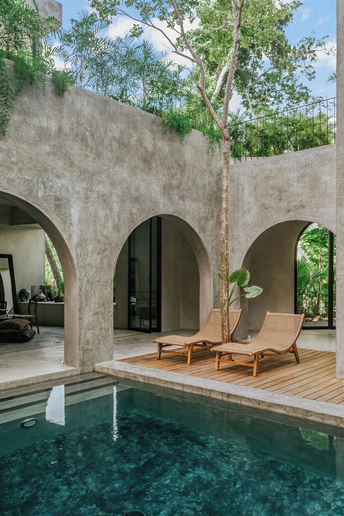 Zona de piscina con agua cristalina, rodeada de arcos de hormigón y amueblada con sillones de mimbre.
