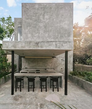 A modern outdoor dining area with a concrete table and stools, surrounded by greenery. - Casa Shalva with Chef & Transportation Included. Two Pools. (Tulum)