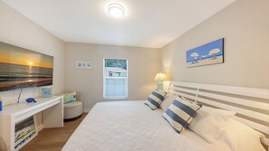Ein Schlafzimmer mit Bett, Schreibtisch, Fenster und Kunstwerken an den Wänden.