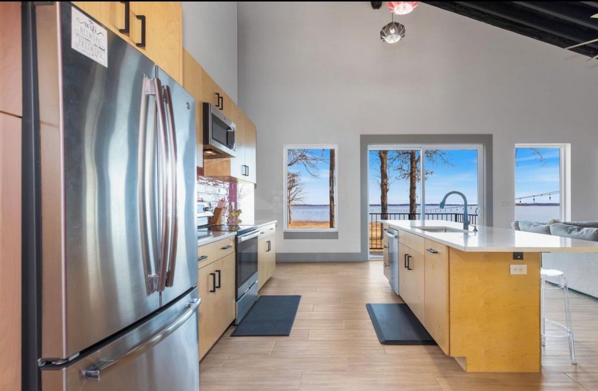 A modern kitchen with a stainless steel refrigerator, wooden cabinets, and a large island with a sink.