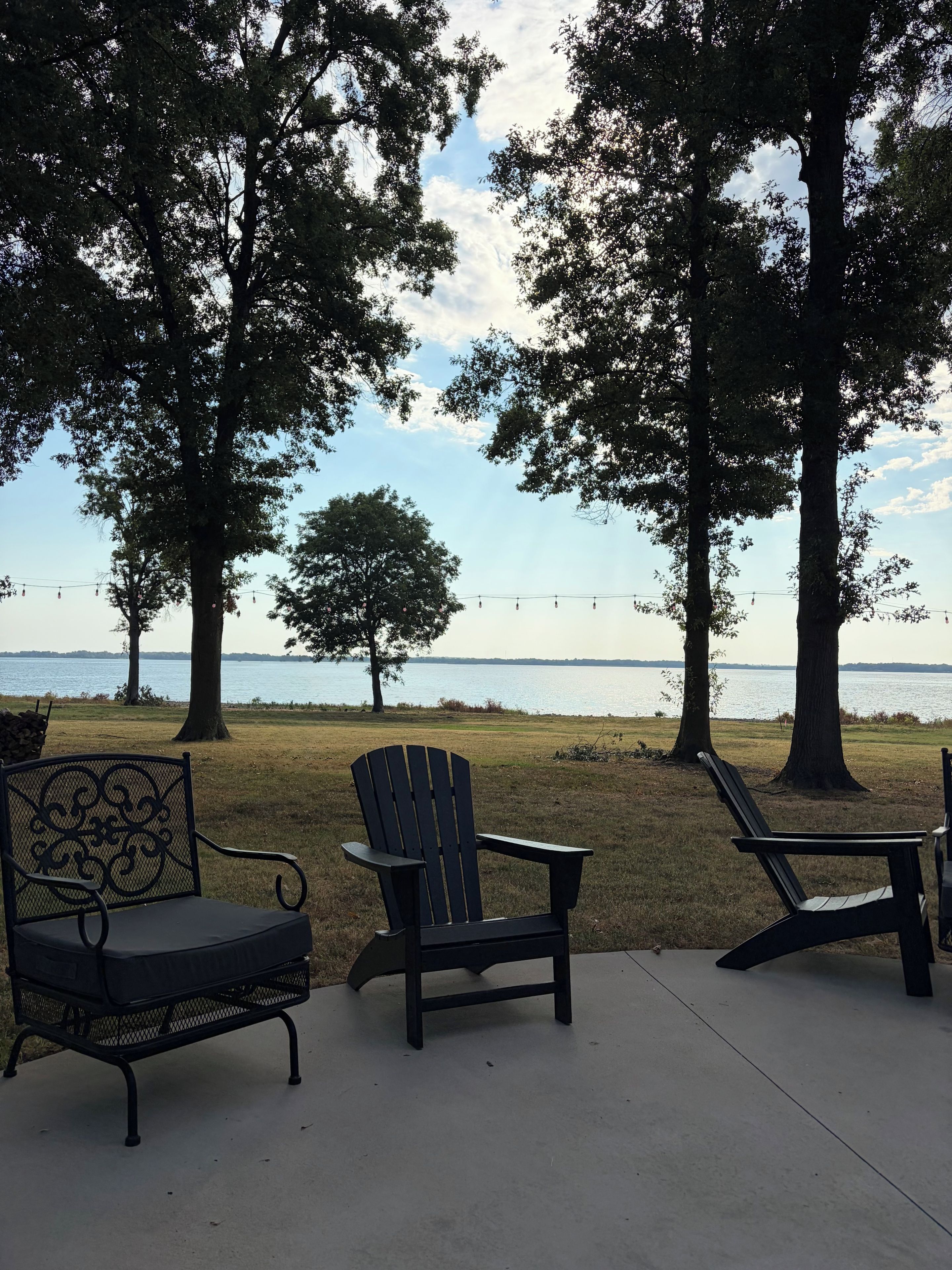 A lakeside seating area with Adirondack chairs and a metal bench, overlooking a calm body of water.