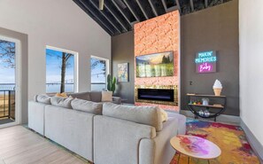 A modern living room with a sectional sofa, a fireplace, and a neon sign.