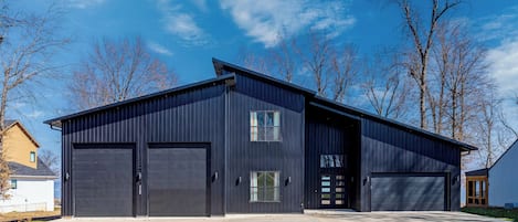 A modern two-story building with a dark exterior, large garage doors, and a flat roof.