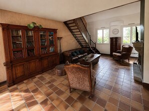 A spacious living room with a large wooden bookcase, a leather sofa, a coffee table, and a staircase leading to another level.