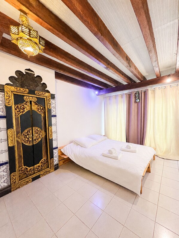 A hotel room with a bed, curtains, a decorative door, and a ceiling light fixture.