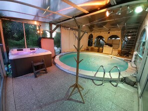 A hot tub and a swimming pool inside a covered area with a view of trees.