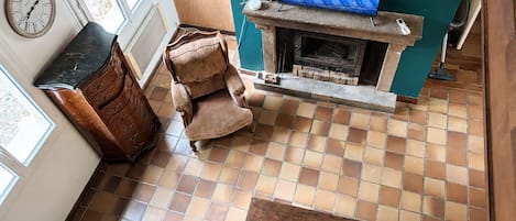 Una sala de estar con chimenea, televisor, reloj y ventana.