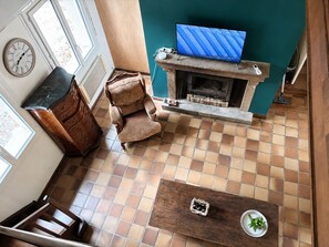A living room with a fireplace, a television, a clock, and a window.