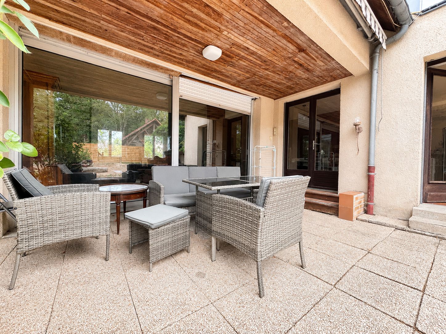 An outdoor patio with wicker furniture, a table, and a ceiling with wooden beams.