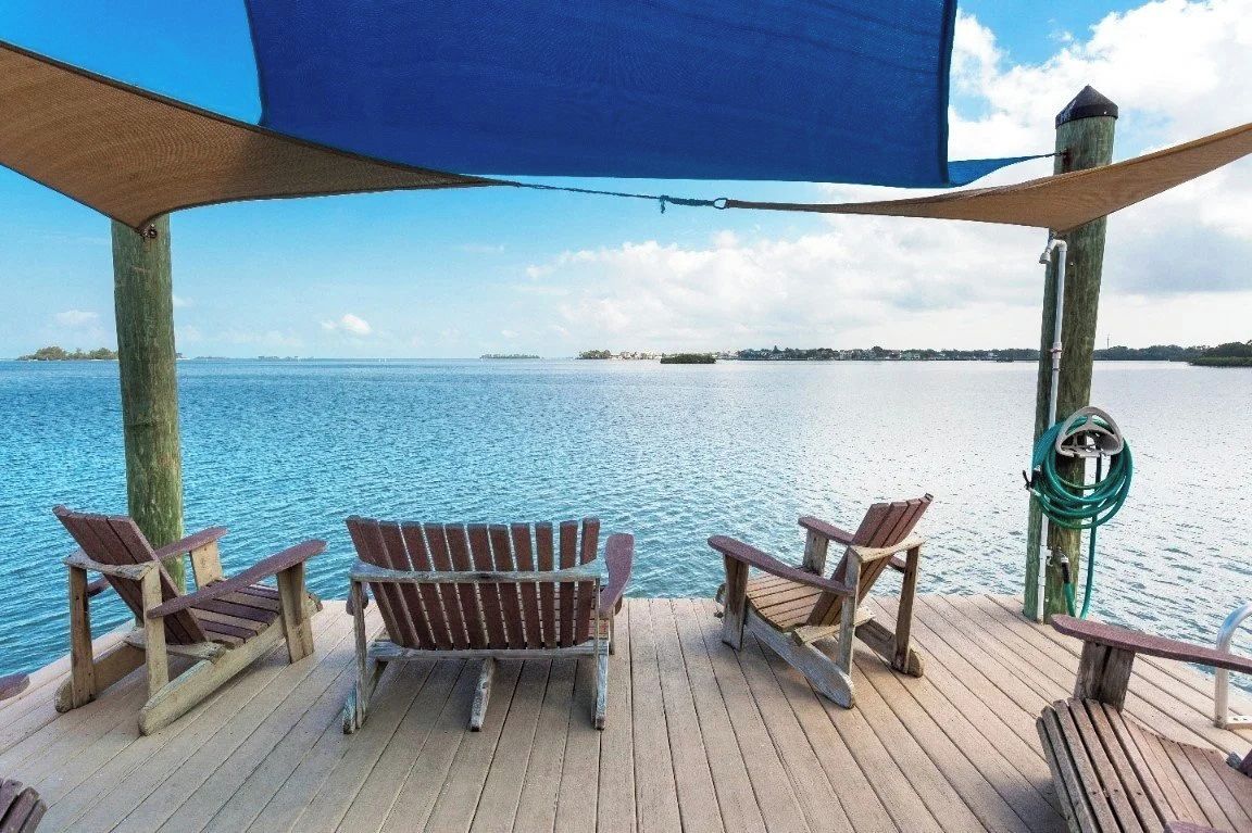 A wooden deck with Adirondack chairs overlooking a calm body of water.