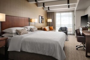 Een hotelkamer met een groot bed, een bureau met een computer, een televisie en een raam met gordijnen.