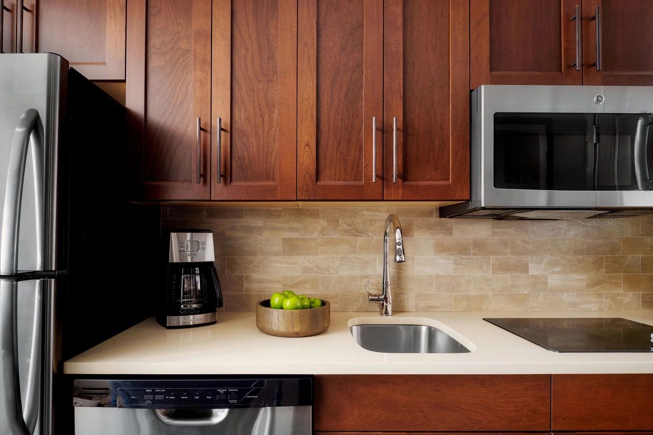 Una cocina con armarios de madera, un refrigerador de acero inoxidable, un microondas, una cafetera y un lavamanos.