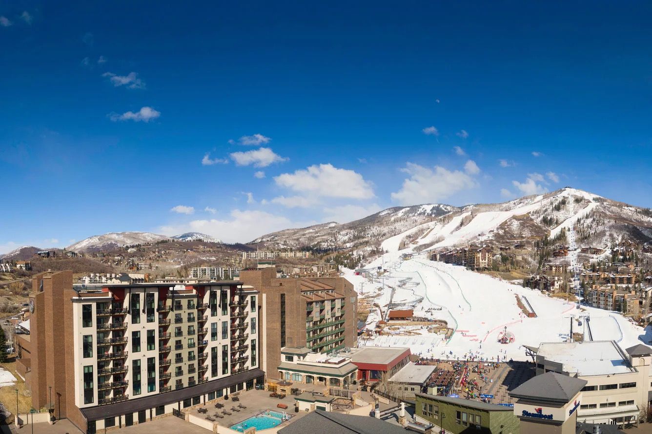Ein Hotel mit mehreren Etagen, einem Schwimmbad und einer Skipiste im Hintergrund.