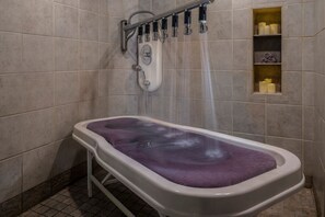 Een bad met een paarse badmat, een douchekop en een plank met toiletartikelen.