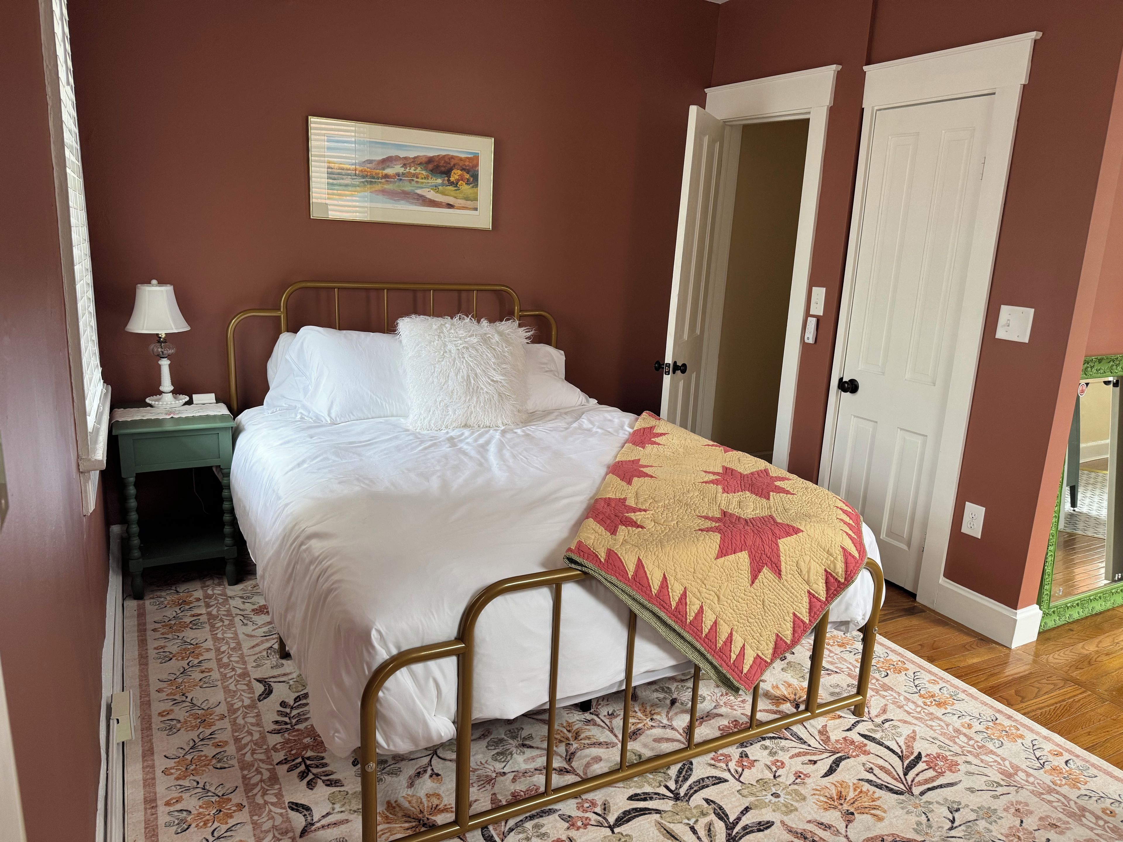Une chambre à coucher avec un lit, une table de chevet, une lampe, un tableau et une porte.