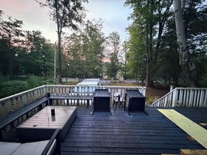 A wooden deck with tables and chairs, surrounded by trees.