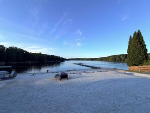 A sandy beach with a boat dock, a wooden fence, and a large tree.