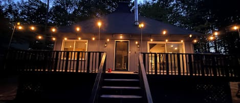 Una pequeña casa con un porche, una escalera que lleva a la entrada y luces colgantes.