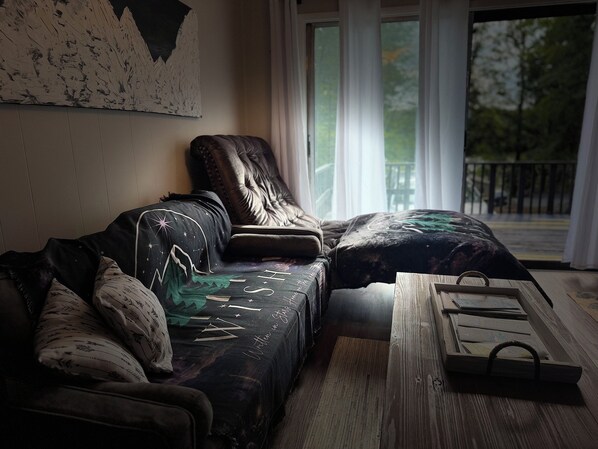 A modern living room with a sofa, a wooden coffee table, and a view of the outdoors through large windows.