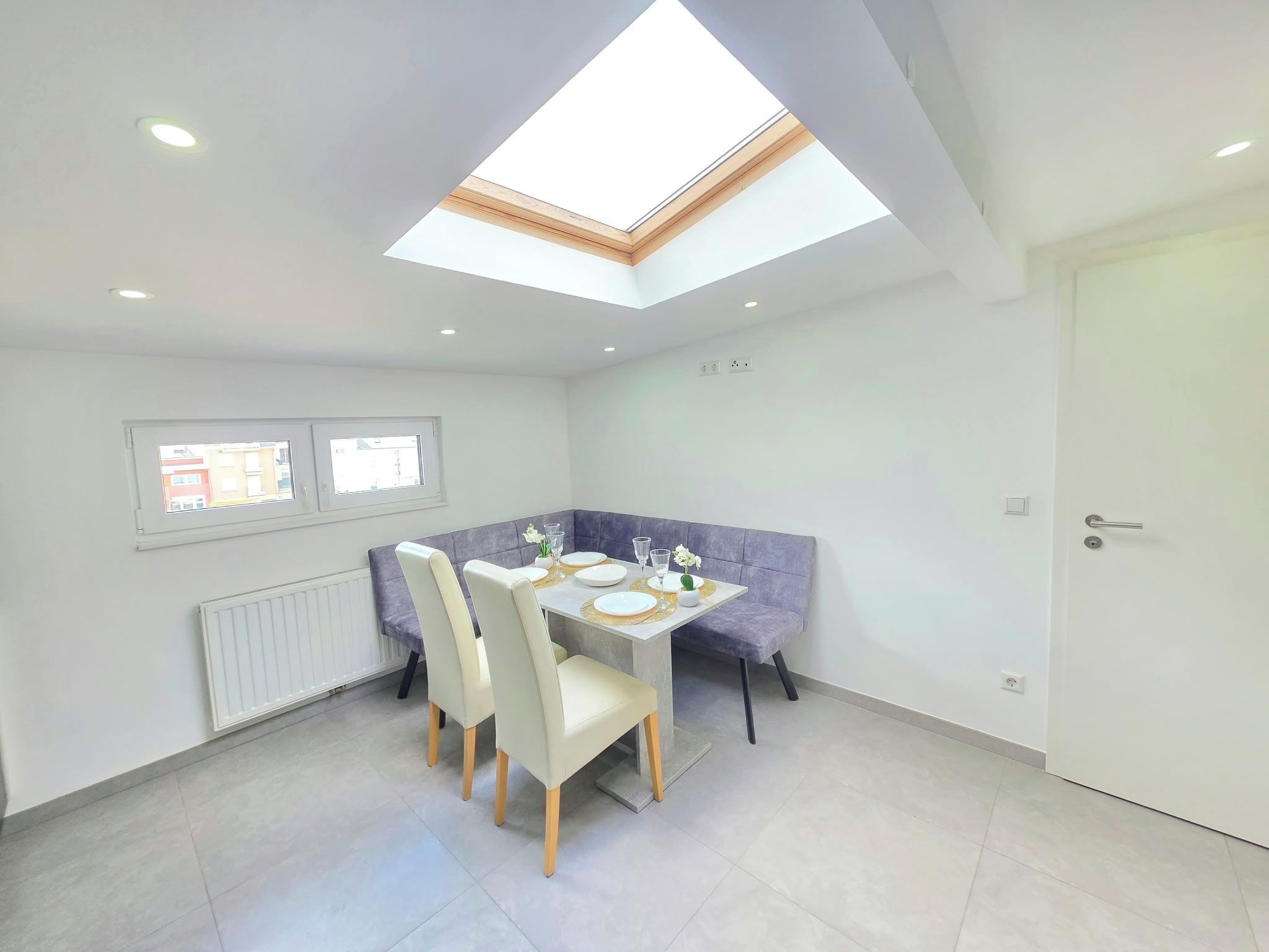 A modern dining area with a skylight, a dining table set for four, and a bench.