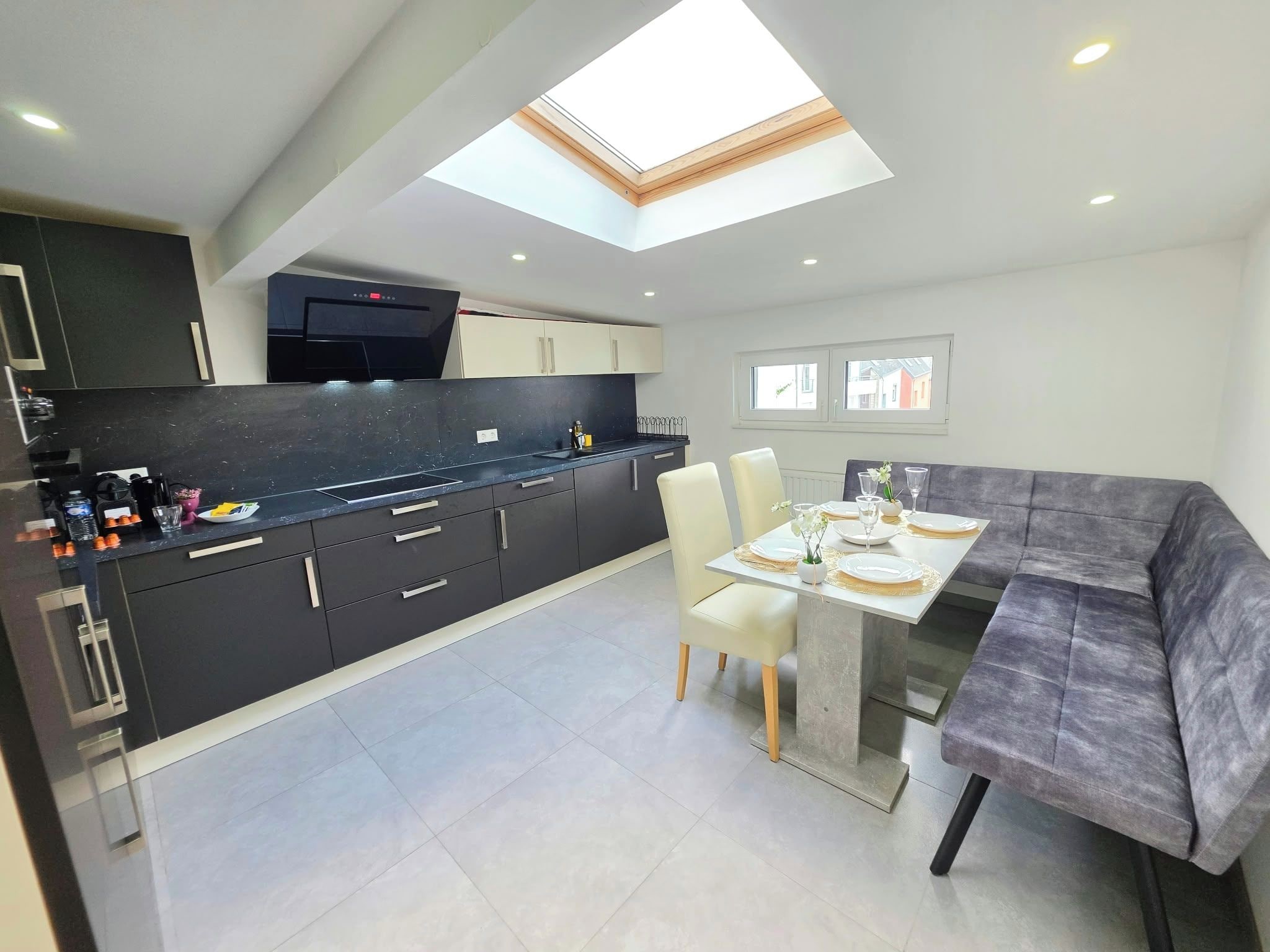 A modern kitchen with a skylight, a dining area with a table set for four, and a grey sofa.