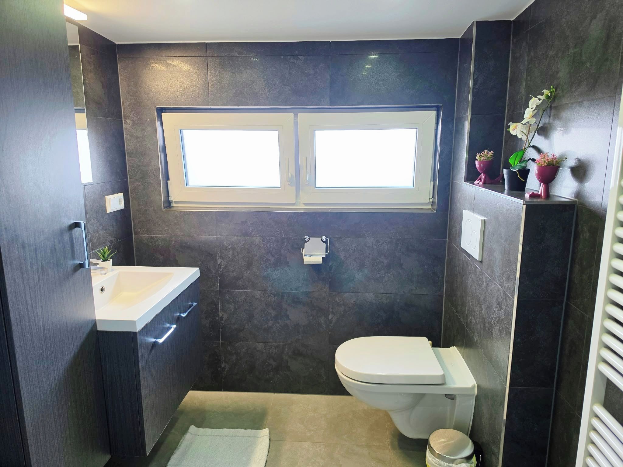 A compact bathroom with a toilet, sink, and a window above the toilet.
