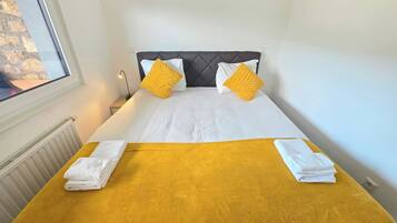 A hotel room with a bed, two pillows, a nightstand, a lamp, and a window.