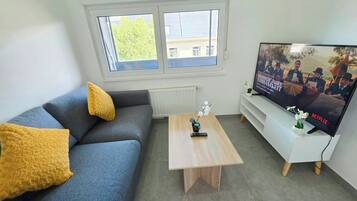 Een woonkamer met een bank, salontafel, televisie en ramen.