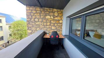 A balcony with a stone wall, a wooden table, and a black chair with red cushions.