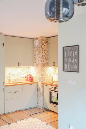 Eine kleine Küche mit gemustertem Fliesenspiegel, einem Backofen und einem gerahmten Pflanzenmotiv an der Wand.