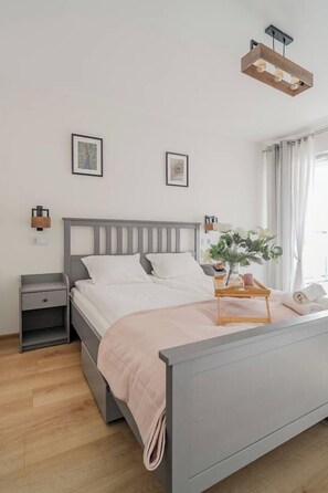 Ein ordentlich bezogenes Bett mit Holz-Kopfteil, ein Nachttisch mit einer Lampe und ein kleiner Beistelltisch.