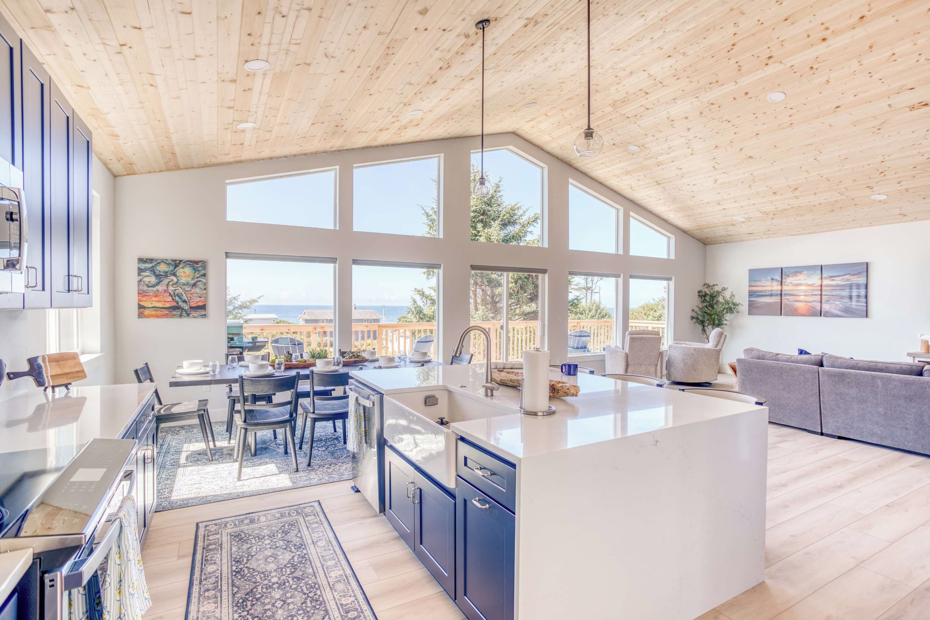 A spacious kitchen with a large island, a dining area, and a view of the sea through large windows.