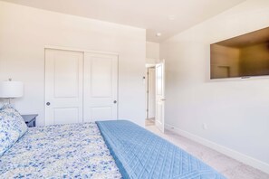 Quarto com cama, mesa de cabeceira, luminária, armário e televisão na parede.