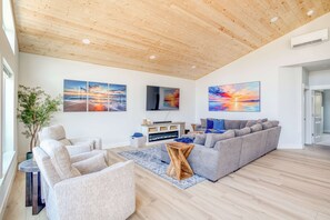 Uma sala de estar moderna com teto de madeira, um sofá modular cinza, uma mesinha de centro e uma janela grande.