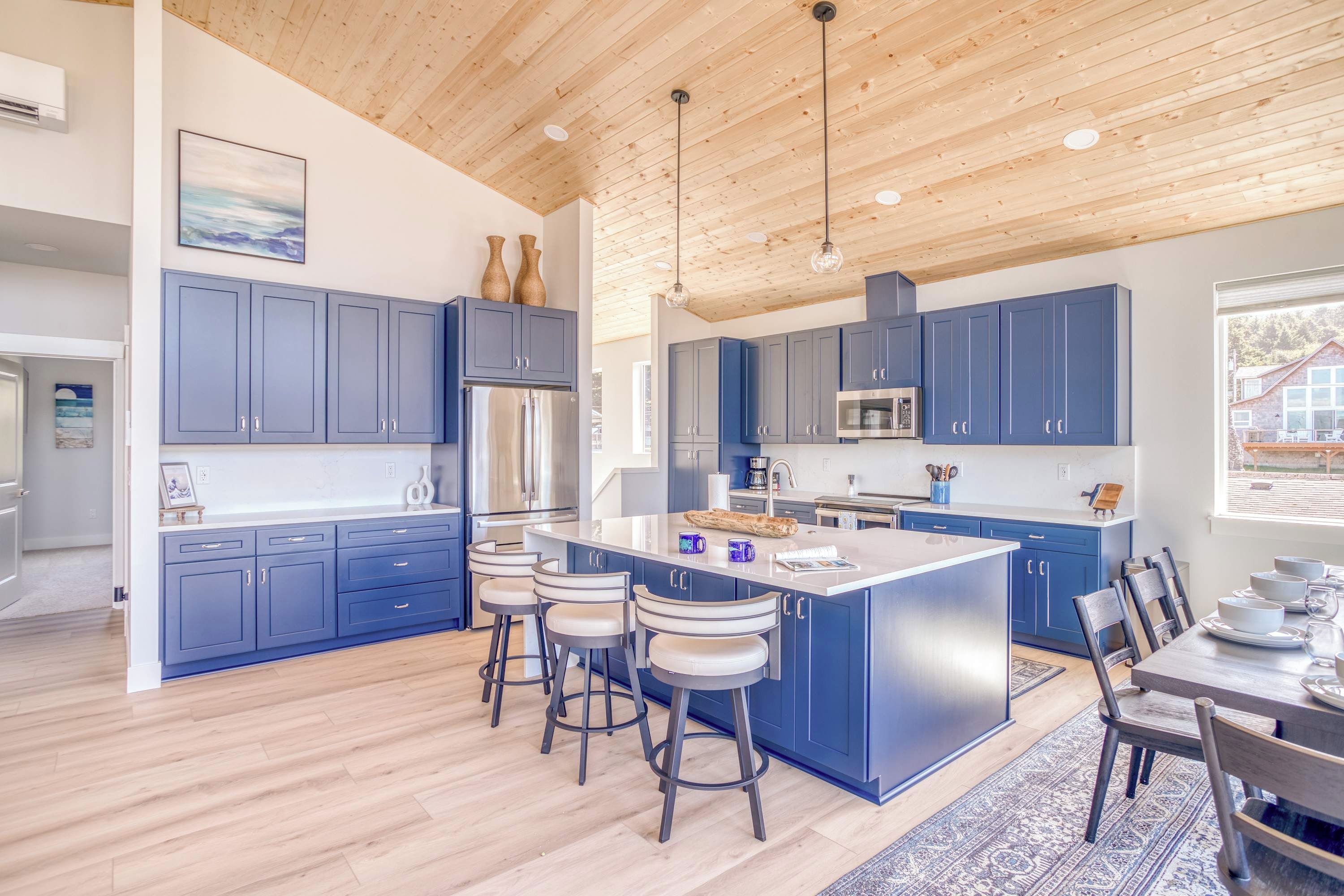 A modern kitchen with blue cabinets, a central island with bar stools, stainless steel appliances, and a wooden ceiling.