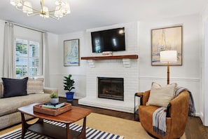 A living room with a fireplace, a sofa, a coffee table, and a television mounted above the fireplace. - 4BR Savannah Retreat | Private Pool, Grill & Garden (Savannah)