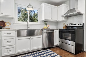 A modern kitchen with white cabinetry, stainless steel appliances, and a blue patterned rug. - 4BR Savannah Retreat | Private Pool, Grill & Garden (Savannah)