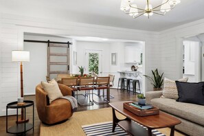 A spacious living room with a brown leather sofa, a coffee table, and a dining area with wicker chairs. - 4BR Savannah Retreat | Private Pool, Grill & Garden (Savannah)