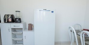 Een kitchenette met een koelkast, koffiezetapparaat, blender en waterkoker.
