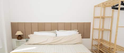 A bed with a headboard, a bedside table with a lamp, and a wooden rack.