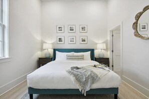 A bedroom with a bed, two bedside tables, a door, and a wall with framed pictures. - Coastal Retreat, Downtown Bay St Louis (Bay St. Louis)