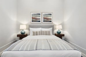 A neatly made bed with a striped blanket, two bedside lamps, and two framed pictures on the wall. - Coastal Retreat, Downtown Bay St Louis (Bay St. Louis)