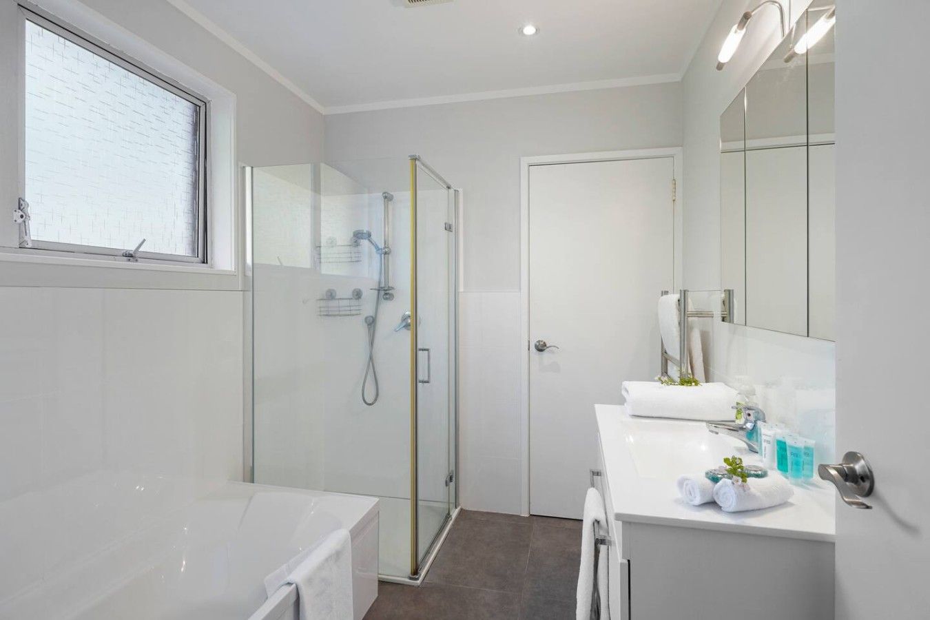 A modern bathroom with a glass-enclosed shower, a white bathtub, and a vanity with a mirror.