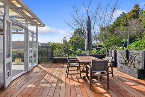 Une terrasse extérieure avec une table et des chaises en bois, entourée de verdure et d’une clôture en bois.