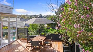 A wooden deck with a table and chairs, surrounded by greenery and a flowering tree.