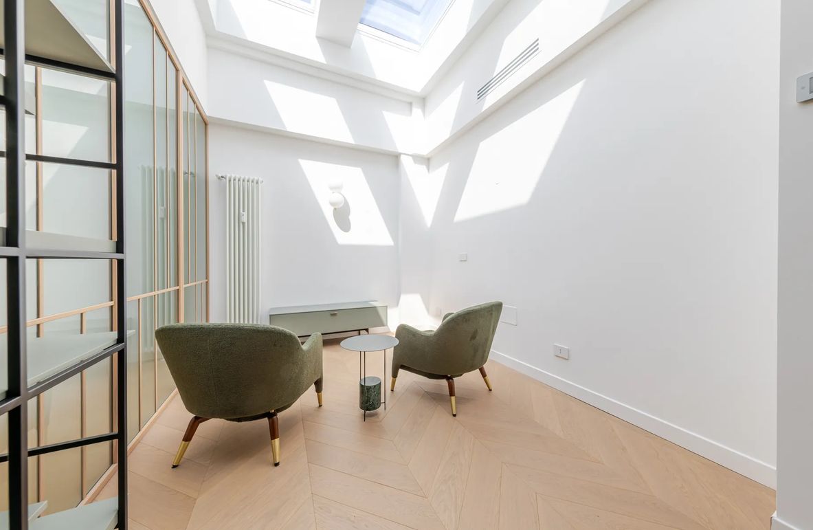 Un intérieur moderne avec une lucarne, deux fauteuils, une petite table et un radiateur.