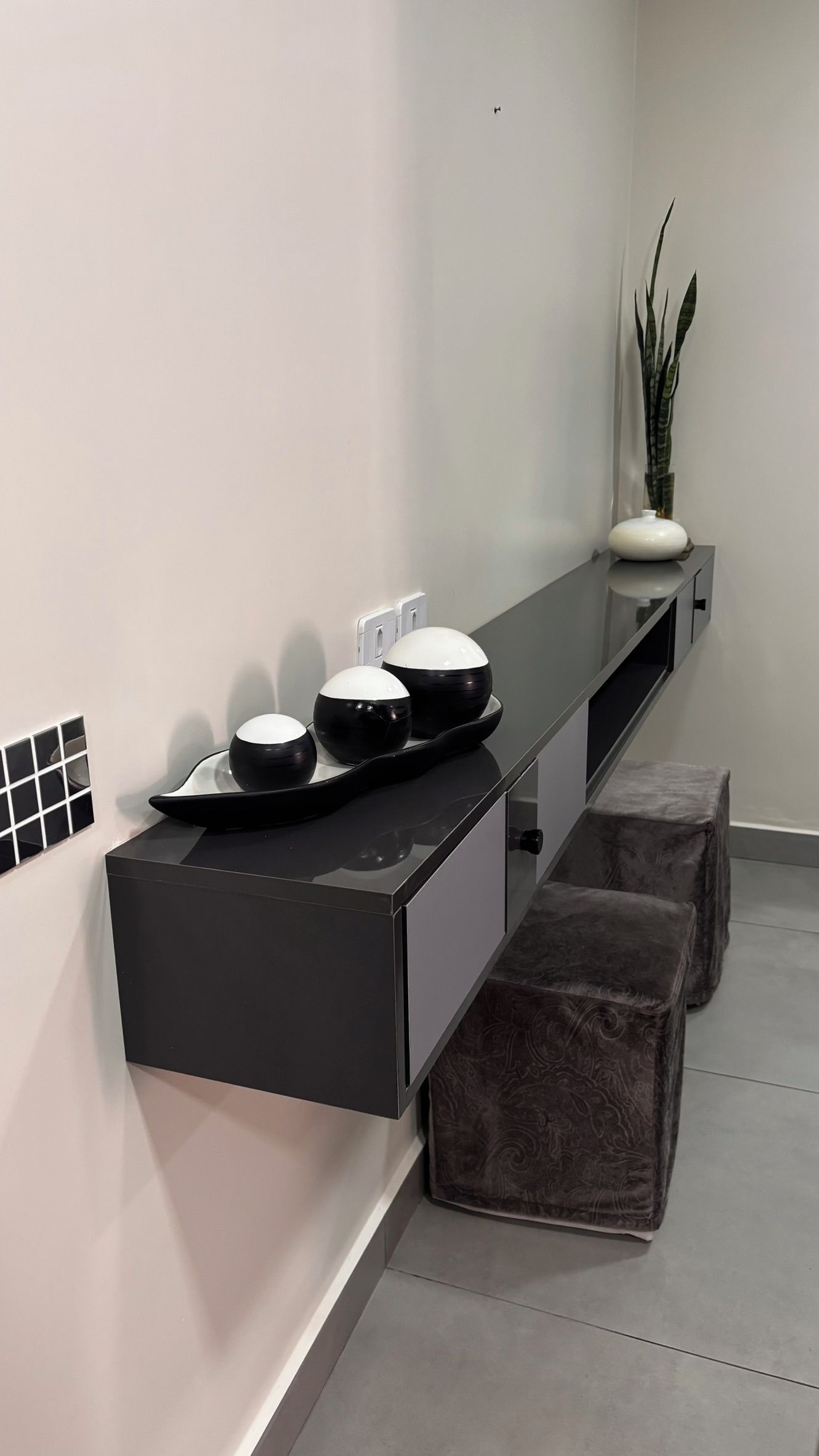 Un bagno moderno con un piano d'appoggio nero, tre lavabi, una pianta in vaso e due pouf.