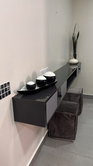 Un baño moderno con encimera negra, tres lavamanos, una planta en maceta y dos otomanas.