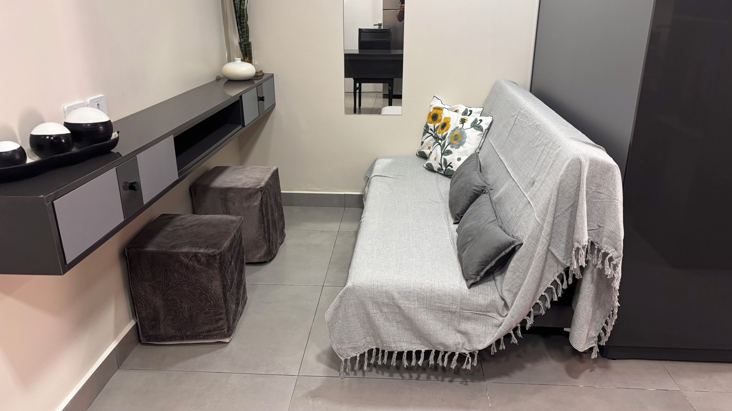 Una sala de estar moderna con un sofá gris, dos otomanas, una mesita y un espejo.