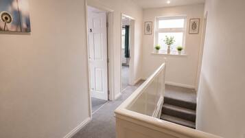 A hallway with a carpeted staircase, a door labeled '5', and a window with plants.